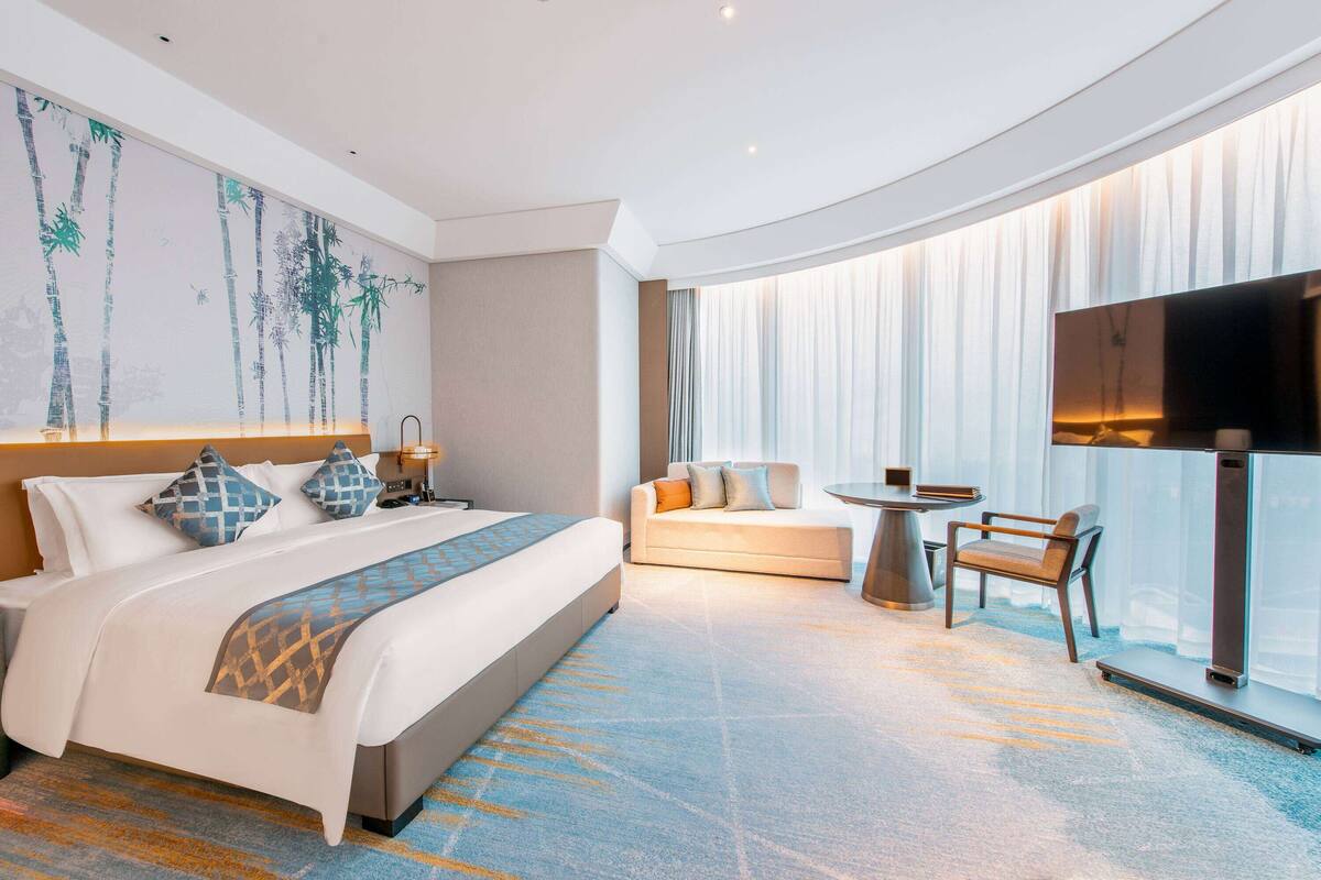 Ein modernes Hotelzimmer mit einem großen Bett, einer Sitzecke, einem kleinen Tisch und einem Fernseher.