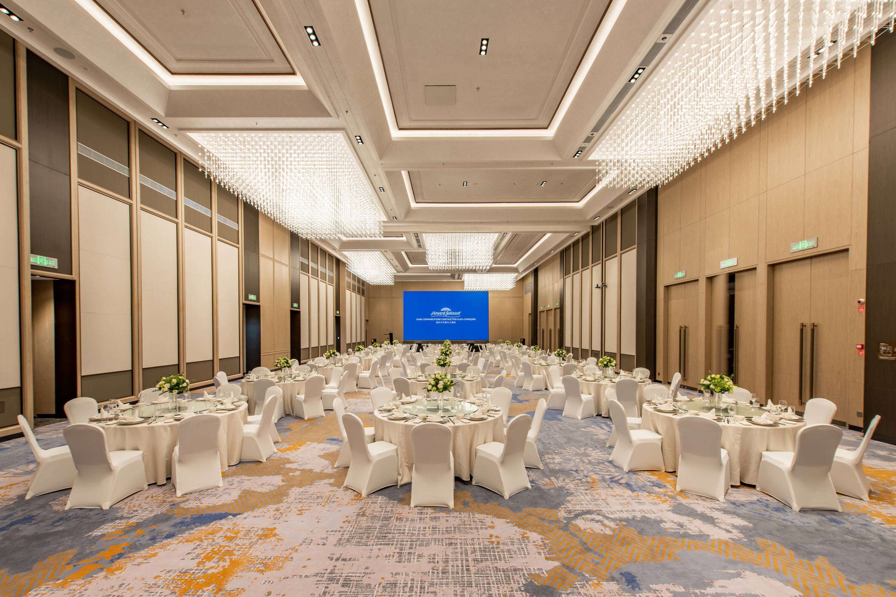 A conference room with round tables, white chairs, and a large screen at the front.