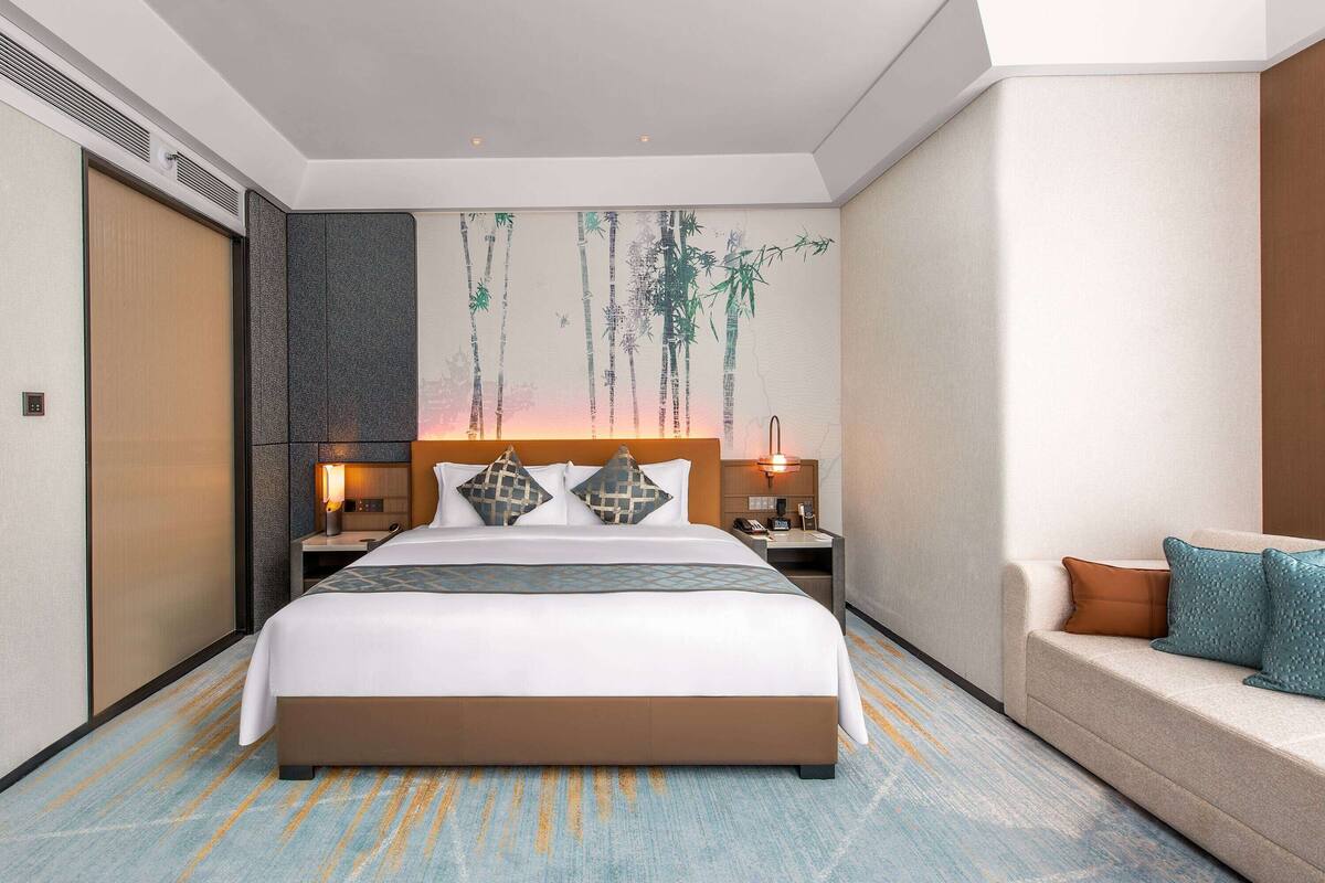 Ein modernes Hotelzimmer mit einem großen Bett, einer Couch, einem Nachttisch und einer Wand mit einem Bambusgemälde.