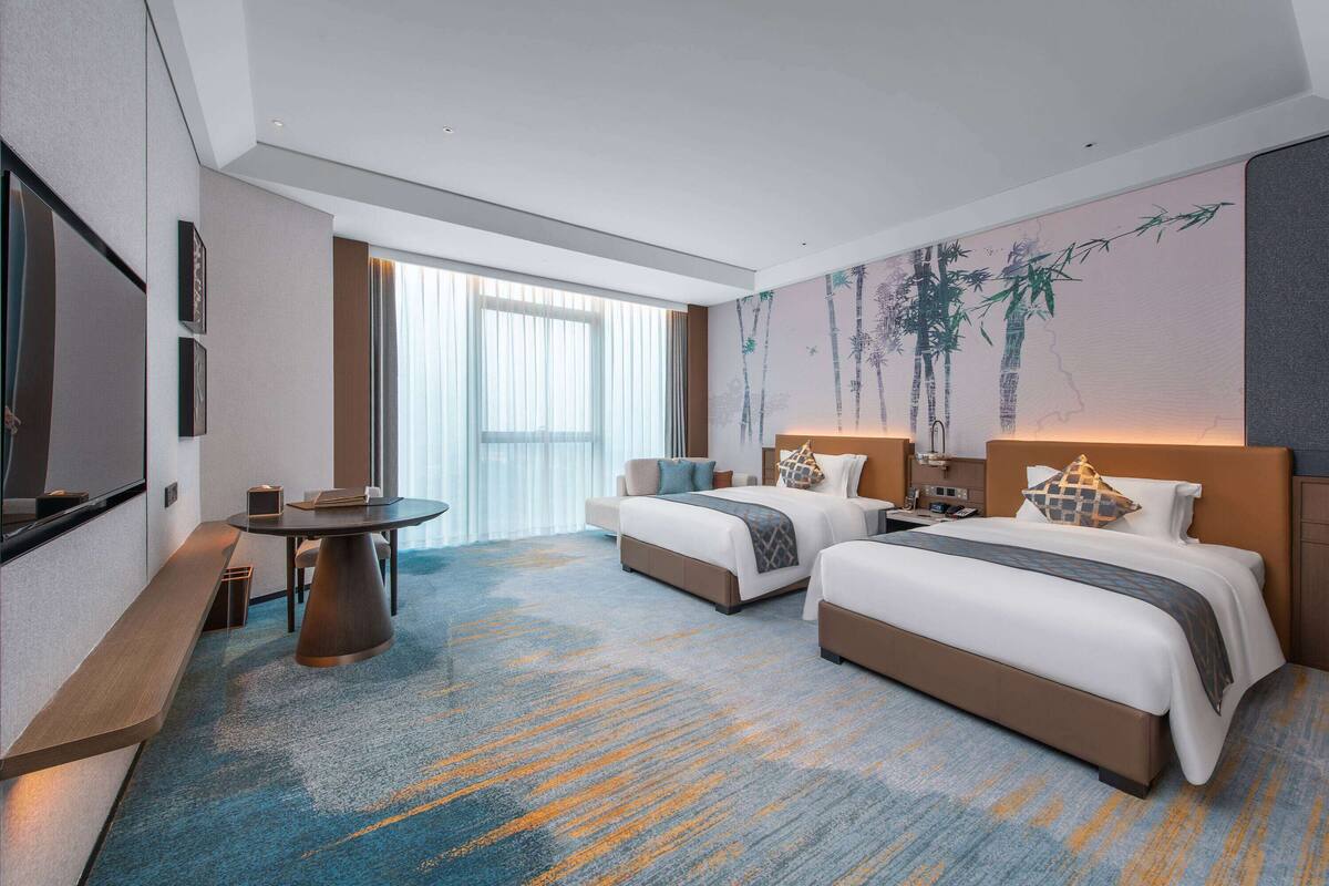 Ein Hotelzimmer mit zwei Betten, einem Schreibtisch und einem großen Fenster.