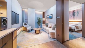 A modern hotel room with a sofa, armchair, and a small coffee table. There is a TV mounted on the wall and a bed with a blue and brown patterned bedspread. - HOJO China Communications Construction Plaza Chongqing (Chongqing)