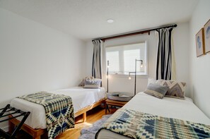 A bedroom with two single beds, a window with blinds, a bedside table with a lamp, and a hanging curtain. - Luxury Home on Blue Ribbon Madison River and steps away from downtown Ennis, MT. (Ennis)