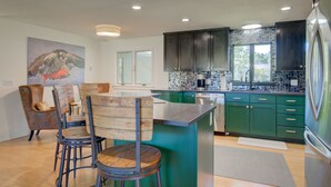 Une cuisine moderne avec des meubles de couleur verte, des appareils en acier inoxydable et un coin repas comprenant des chaises et une table en bois.