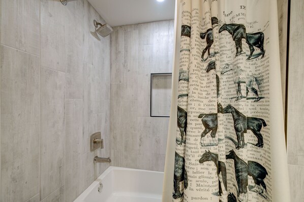 A bathroom with a bathtub, a shower, and a curtain with horse illustrations.