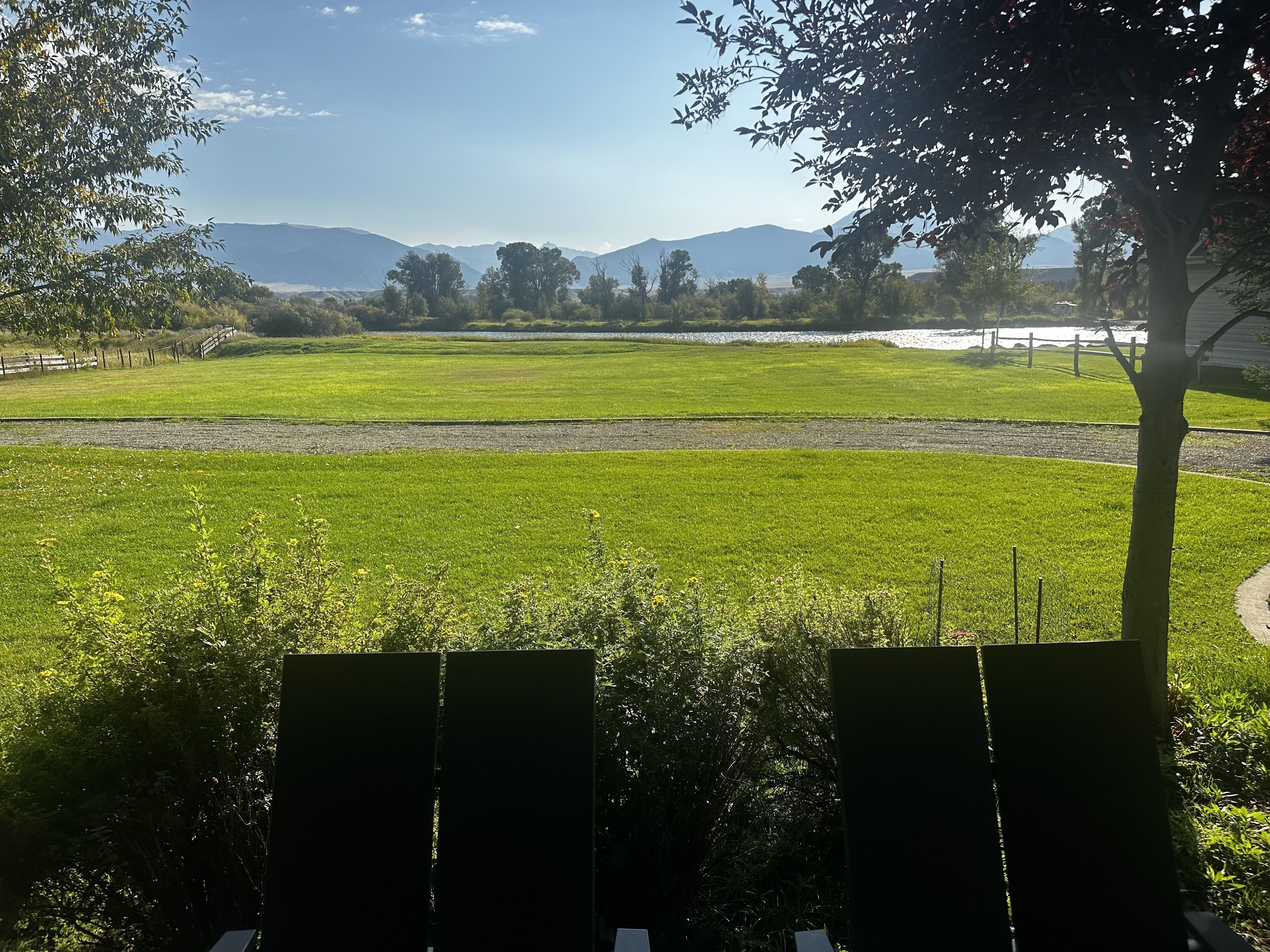 A grassy field with a fence and trees, a path, and distant mountains.