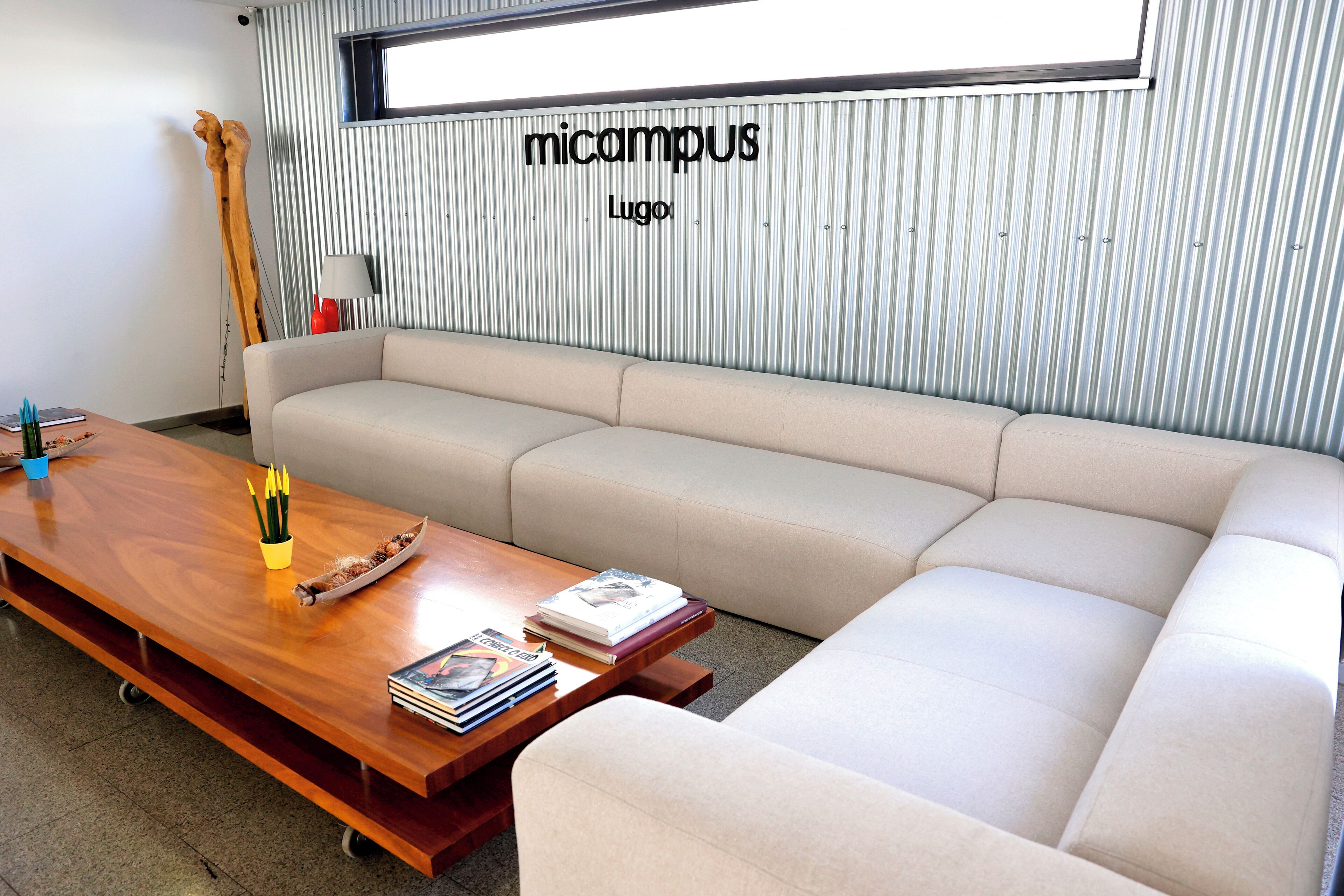 A modern living room with a wooden coffee table, beige sofa, and a striped wall with the text "micampus Lugo".