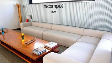 A modern living room with a wooden coffee table, beige sofa, and a striped wall with the text "micampus Lugo".