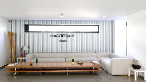 A modern living room with a large sectional sofa, a wooden coffee table with wheels, a small side table, and a potted plant. - Micampus Lugo (Lugo)