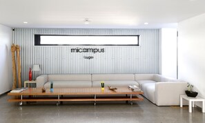 A modern living room with a large sectional sofa, a wooden coffee table with wheels, a small side table, and a potted plant. - Micampus Lugo (Lugo)