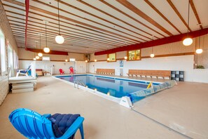 An indoor swimming pool with a wooden ceiling, a blue lounge chair, and a red chair. - Cozy 1BR Lodge – Fall & Winter Retreat in Jackman (Jackman)
