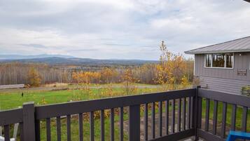 A wooden deck with a view of a grassy field and trees in autumn colors.