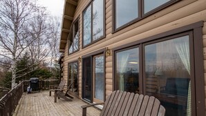 Eine Holzterrasse mit einer Bank, einem Grill und Blick auf ein Gebäude mit großen Fenstern und einem Balkon.