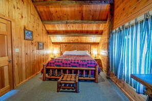 A wooden cabin bedroom with a bed, a bench, and a view of a forest through a window. - North Woods Cabin for 10 with Fireplace, Loft & Whirlpool Tub (Jackman)
