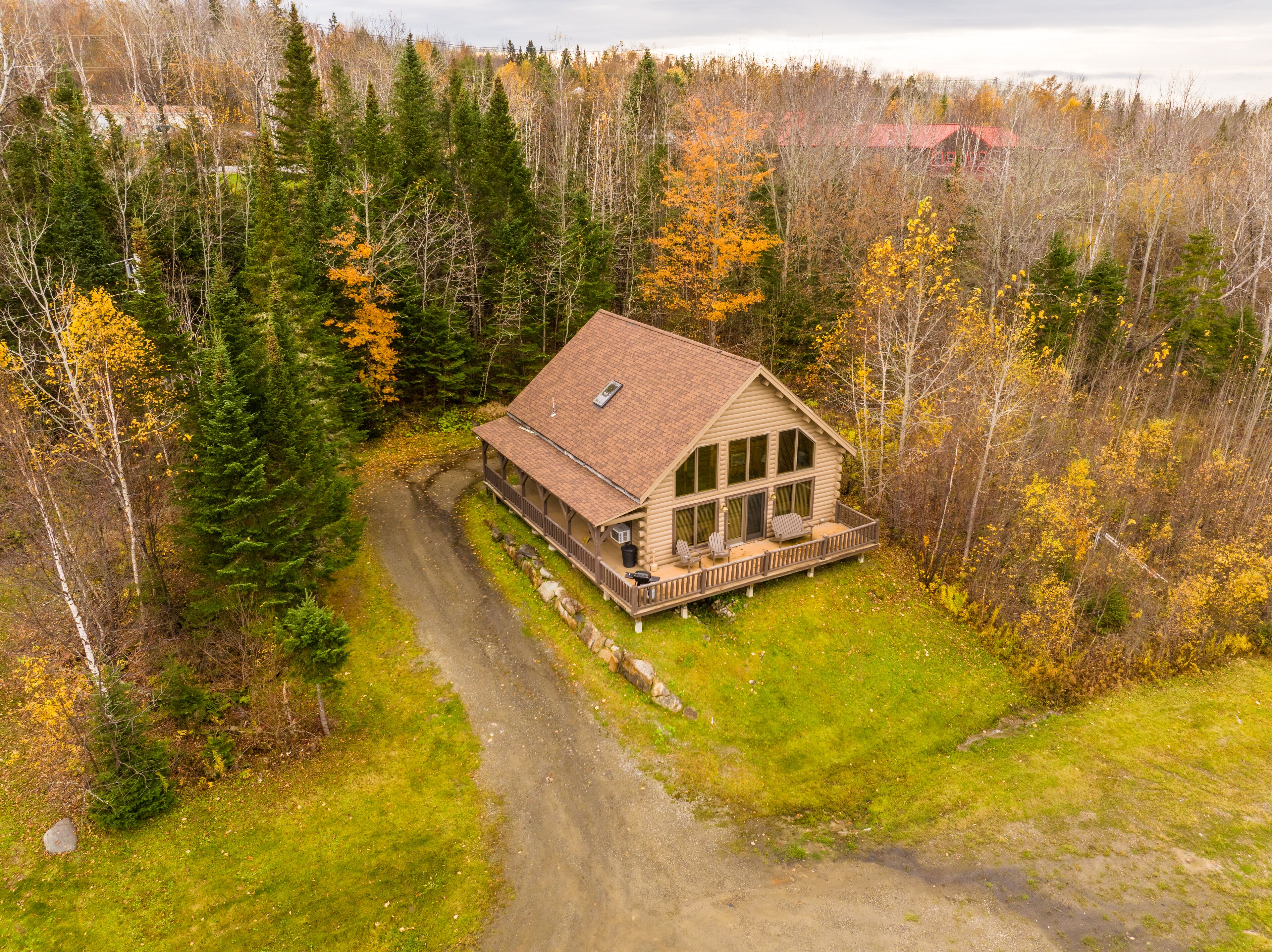 A log cabin with a porch and large windows, surrounded by a forest with autumn foliage.