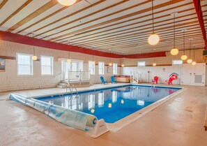 An indoor swimming pool with a clear blue water, surrounded by red and blue chairs, and a wooden ceiling with hanging lights. - North Woods Cabin for 10 with Fireplace, Loft & Whirlpool Tub (Jackman)