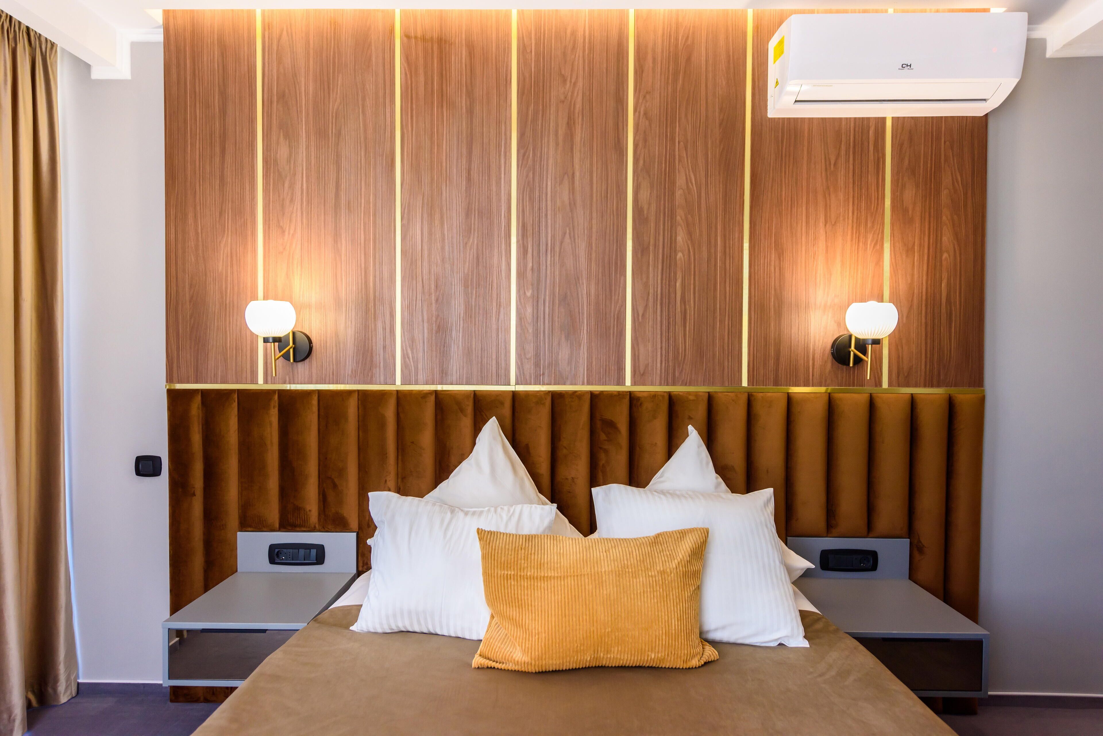 A hotel room with a wooden panel wall, a tufted headboard, a bed with white and yellow pillows, bedside tables, and wall-mounted lamps.