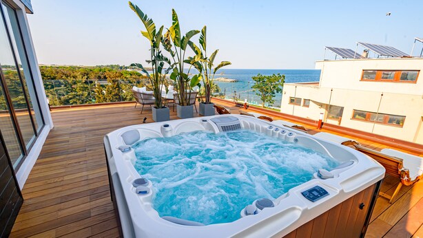 A hot tub on a wooden deck with a view of the sea and greenery.