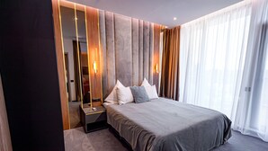 A modern hotel bedroom with a large bed, a nightstand, and a mirror.