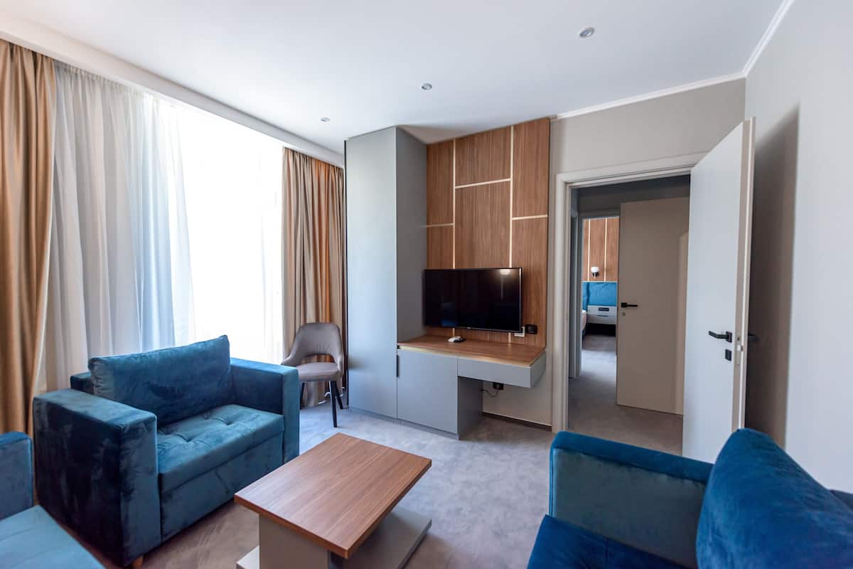 A modern hotel room with a sofa, a chair, a TV, and a desk.