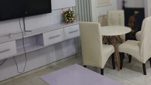 Un salon moderne avec un téléviseur à écran plat fixé au mur, une table basse, deux fauteuils et une petite plante décorative.