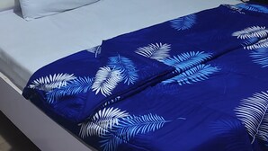 Un lit avec une tête de lit blanche et une couvre-lit bleue ornée de motifs de feuilles blanches.