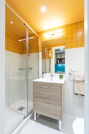 A modern bathroom with a glass-enclosed shower, a wooden vanity with a sink, and a mirror above the vanity. - Micampus Salamanca (Salamanca)
