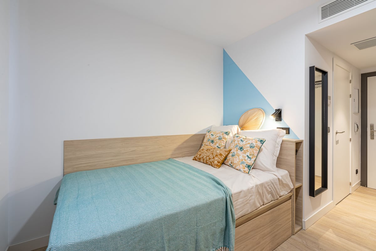 A bedroom with a bed, pillows, a bedside lamp, and a door.