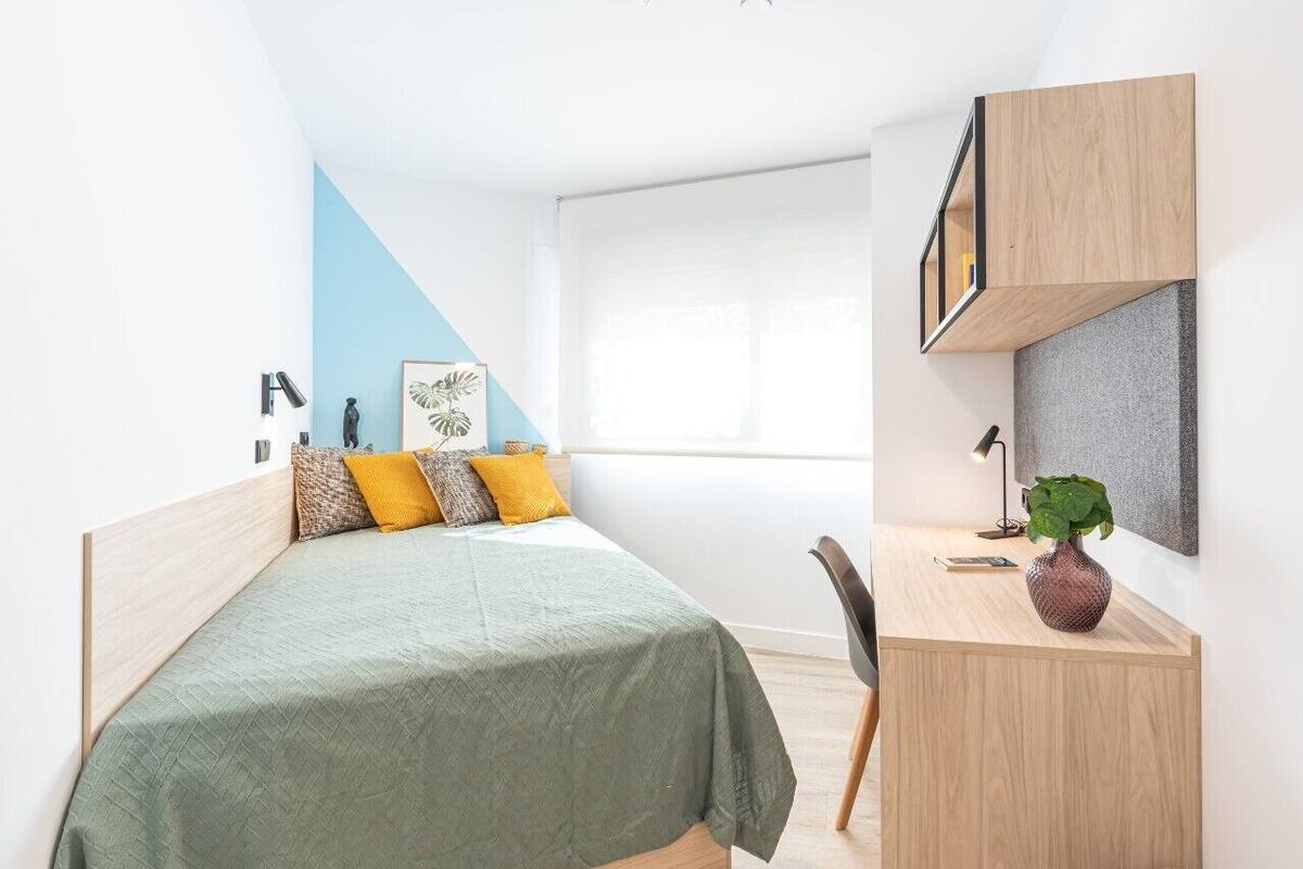 A modern bedroom with a bed, desk, chair, and a potted plant.