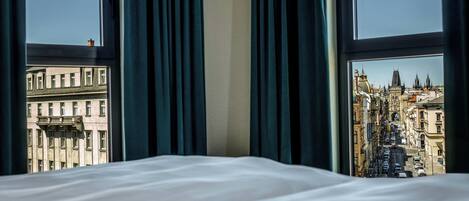 Habitación de hotel con cama, cortinas y vista de un paisaje urbano a través de ventanas amplias.