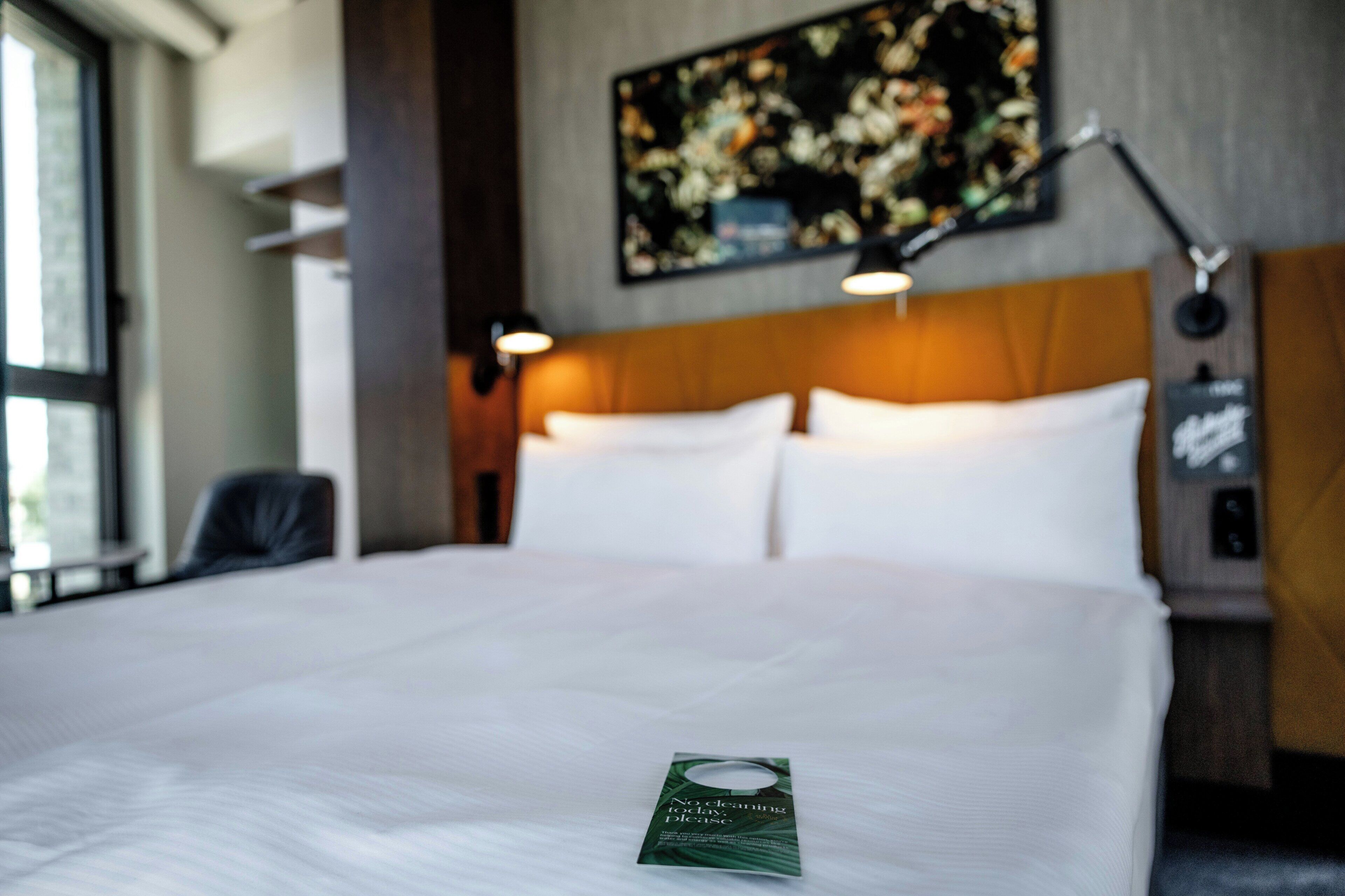 Una habitación de hotel con una cama bien hecha, una obra de arte floral enmarcada en la pared y una mesita de noche con una lámpara.