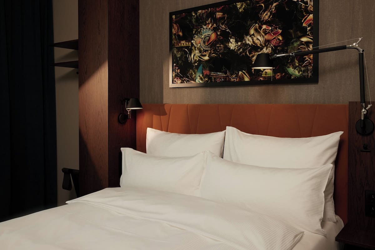 A neatly made bed with white linens, a wooden headboard, and a wall-mounted painting above it.