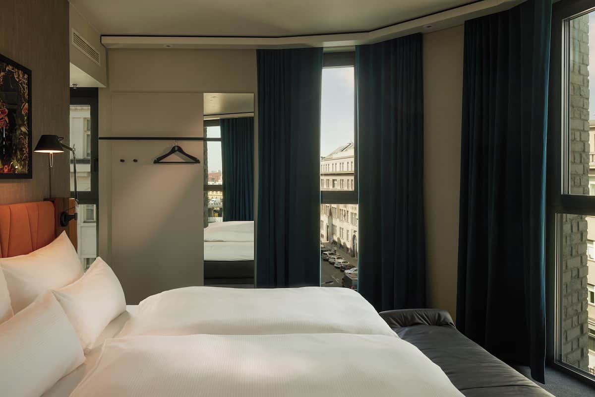 A hotel room with a large bed, a view of a city street, and a mirror reflecting the room.