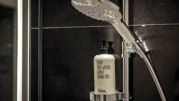 A bathroom with a shower, a soap dispenser, and a tiled wall.