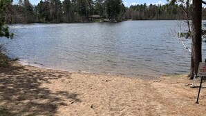 A lakeside view with a sandy beach, a fishing rod, and a house in the background. - Nordic Hideaway on Silverthorn Lake - Little Sisu (Hayward)