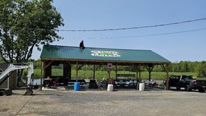 Un pavillon couvert avec un toit végétalisé, une aire de stationnement en gravier et une personne assise sur le toit.