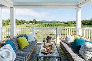 A covered patio with two sofas, a table with food and drinks, and a view of a vineyard. - Fern Cottage Summary: (Gordonsville)