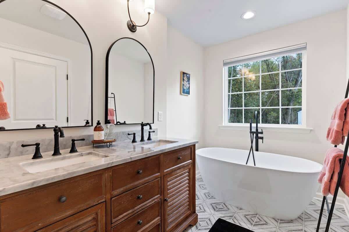 Une salle de bain avec une baignoire sur pieds, un grand miroir et une fenêtre donnant sur les arbres.