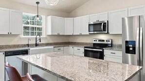 A modern kitchen with white cabinets, granite countertops, stainless steel appliances, and a pendant light.