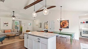 A modern kitchen with white cabinets, a granite countertop, and a dining area with a green table and chairs.