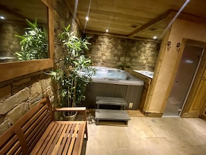 Een wellnessruimte met een bubbelbad, een houten bank, stenen muren en een plant in pot.