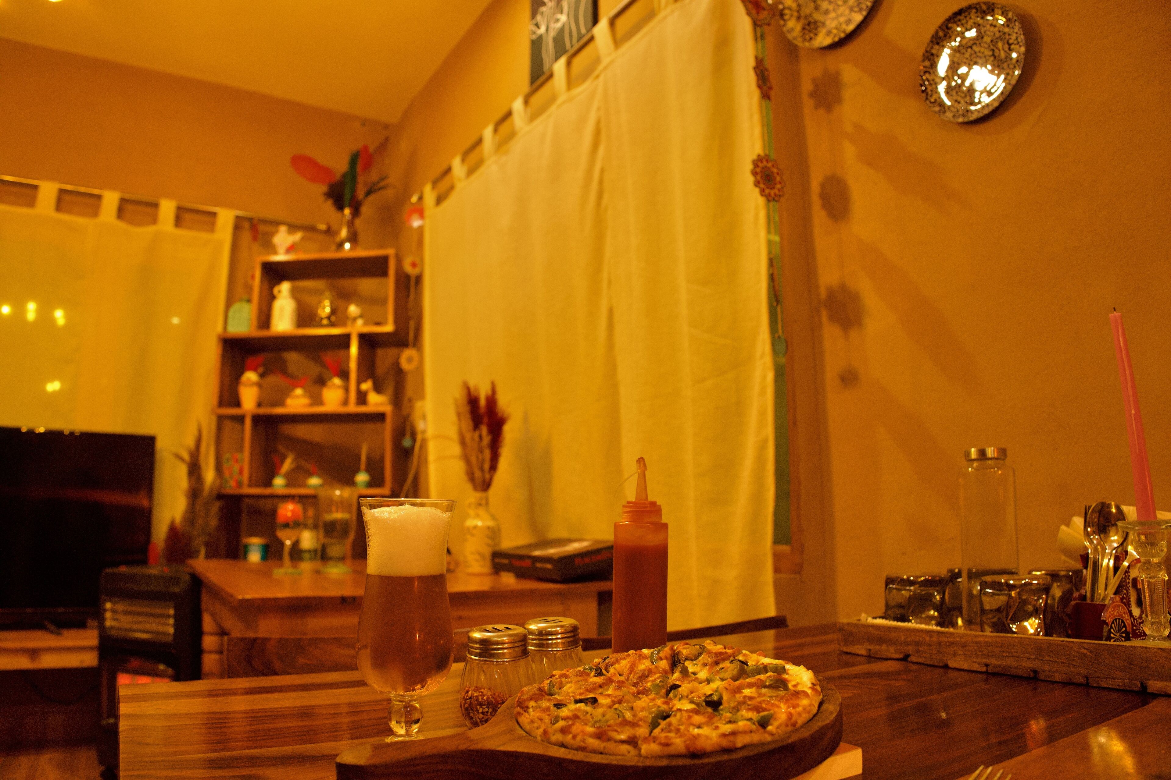 Ein Esstisch mit Pizza, einem Bierglas, Salz- und Pfefferstreuern, einer Ketchupflasche und einer Kerze.