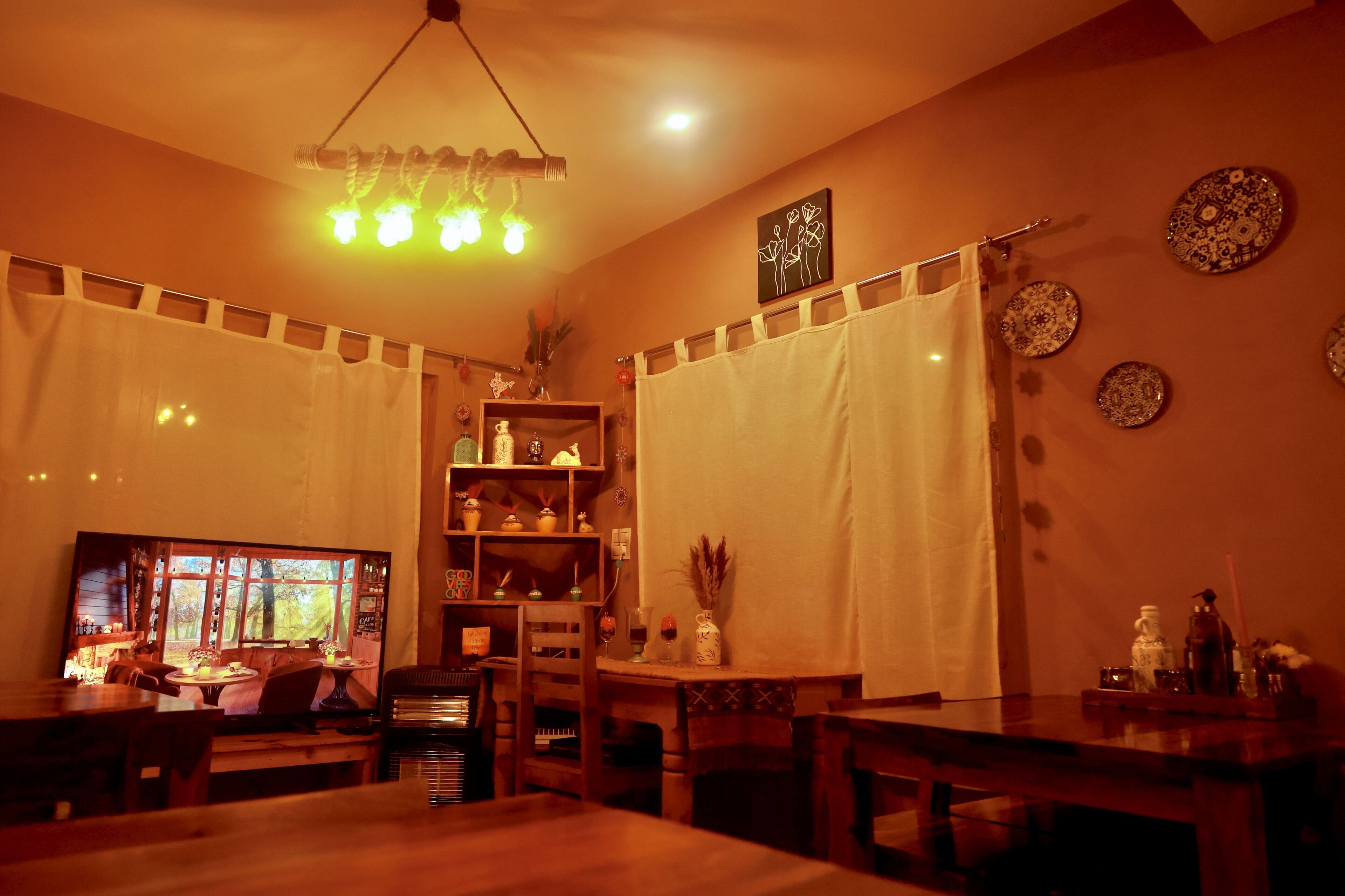 A cozy dining area with a wooden table and chairs, a chandelier, and a window with a view of trees.