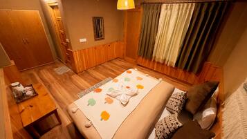 Un dormitorio con suelo de madera, una cama con cubrecama floral, una mesita de noche con lámpara y una ventana con cortinas.