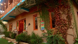 A building with a balcony, ivy-covered walls, and a small garden with orange flowers. - Khwaabgaah-A Boutique Homestay (Banjar)