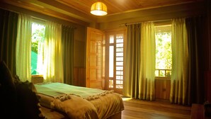 A room with a wooden floor, a bed with a green bedspread, and curtains on the windows. - Khwaabgaah-A Boutique Homestay (Banjar)