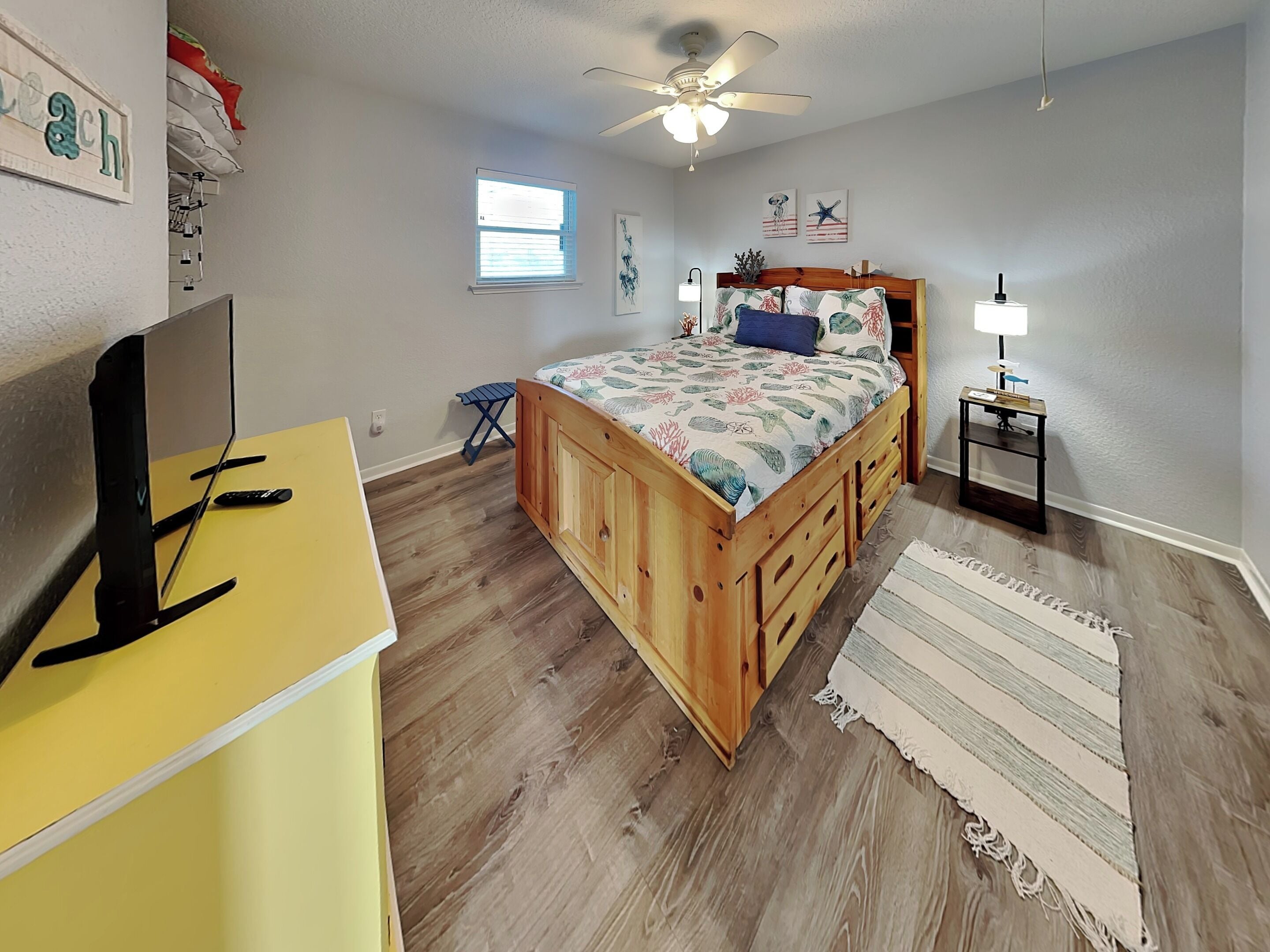 A bedroom with a bed, a desk, a ceiling fan, a window, and a nightstand.