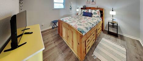 A bedroom with a bed, a desk, a ceiling fan, a window, and a nightstand.