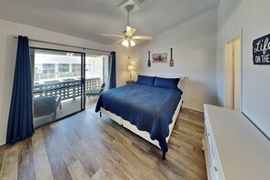 A bedroom with a bed, a ceiling fan, a nightstand, a lamp, a view through a sliding door, and a sign on the wall. - La Buena Vida by Miss Kitty’s (Rockport)