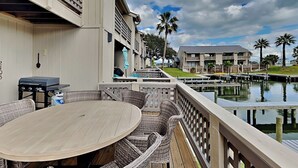 A wooden deck with wicker furniture, overlooking a marina with boats and palm trees. - La Buena Vida by Miss Kitty’s (Rockport)