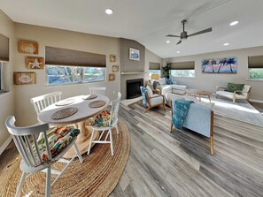 Uma sala de estar moderna com lareira, um espaço de refeições com mesa redonda e uma área de estar com sofá e poltronas.